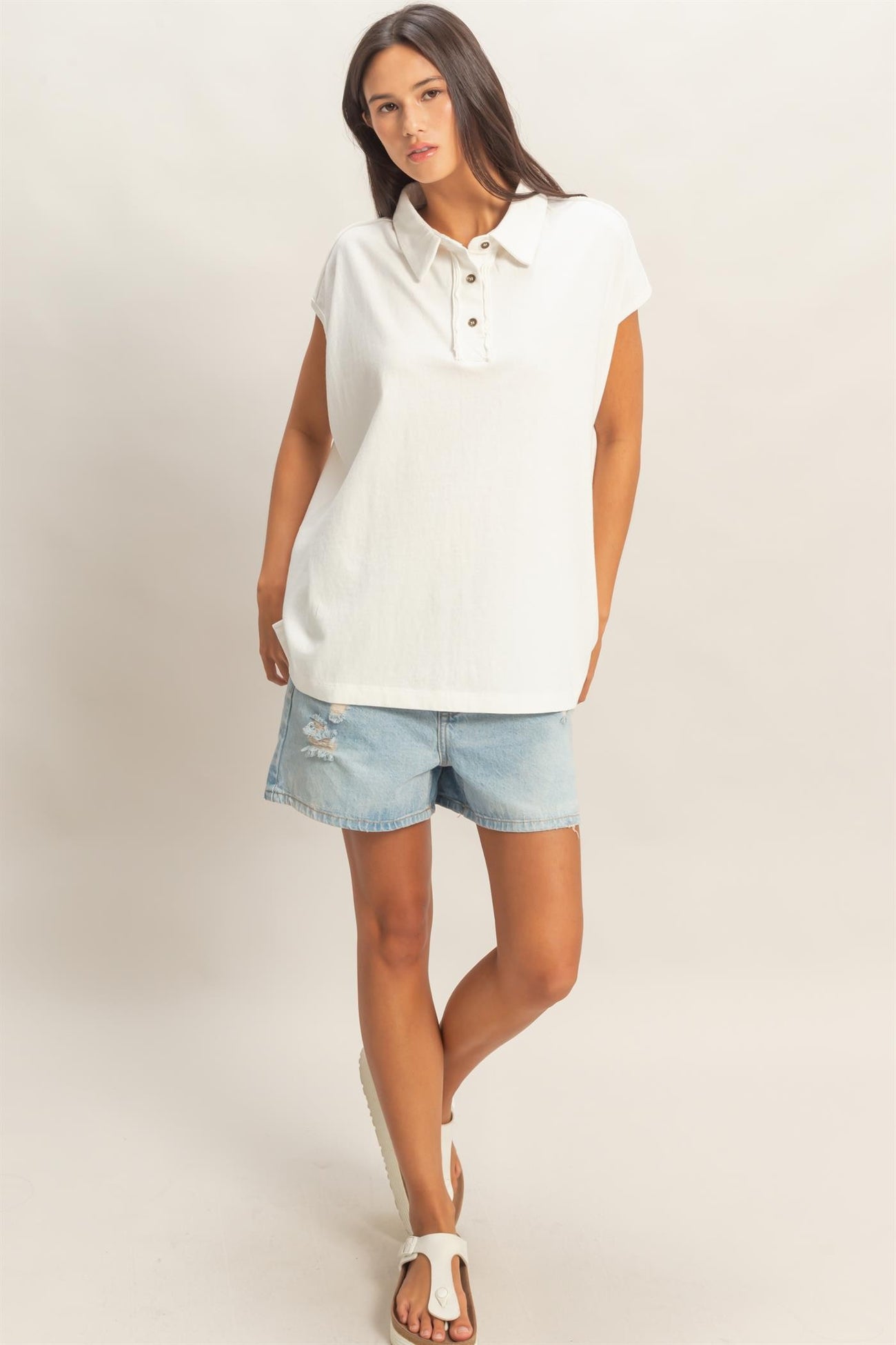 woman wearing a white sleeveless collared top with button details and denim shorts