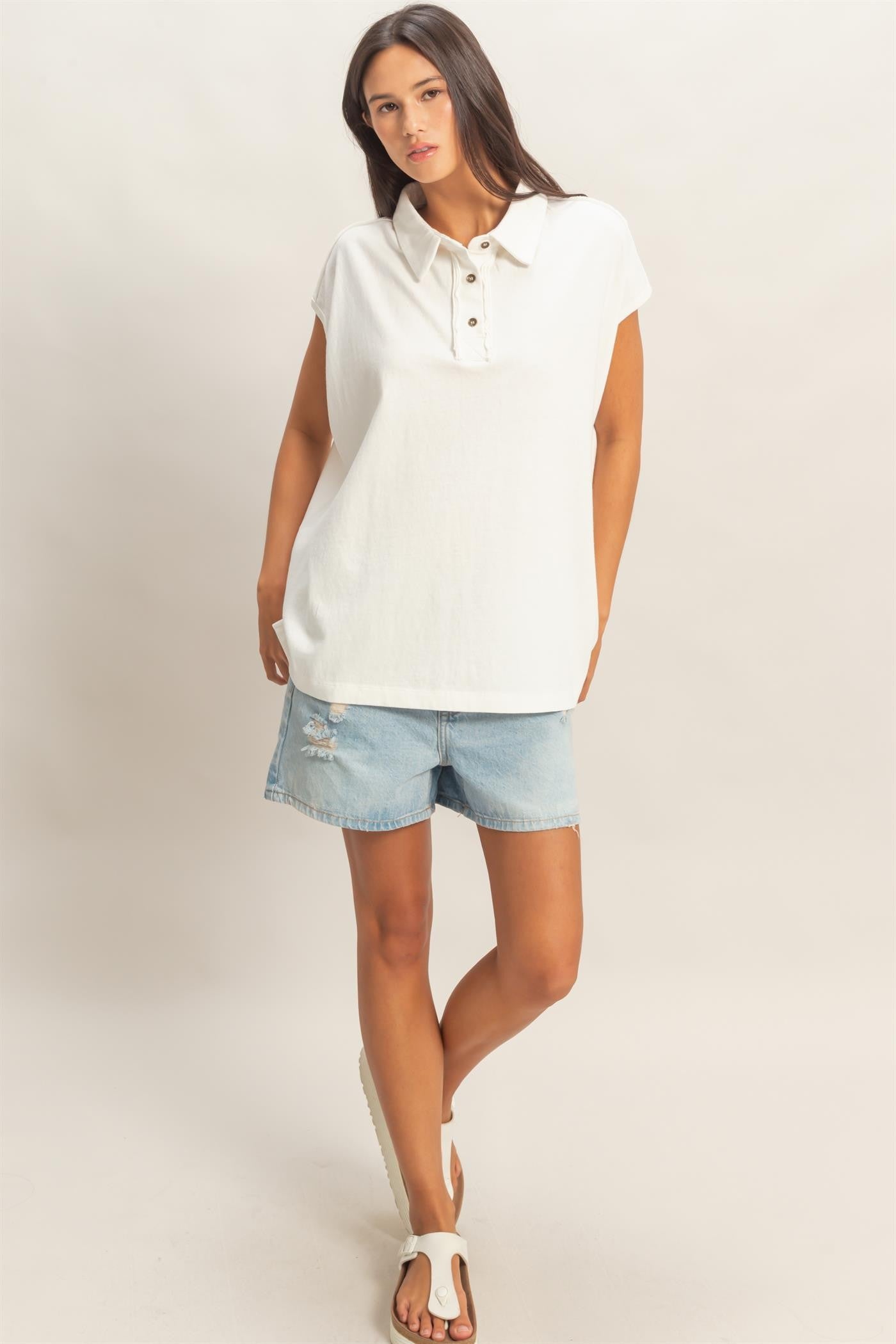 woman wearing a white sleeveless collared top with button details and denim shorts