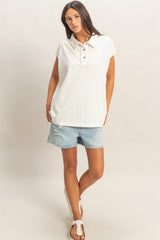 woman wearing a white sleeveless collared top with button details and denim shorts