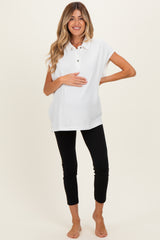 woman wearing a white maternity polo shirt and black leggings, holding her baby bump