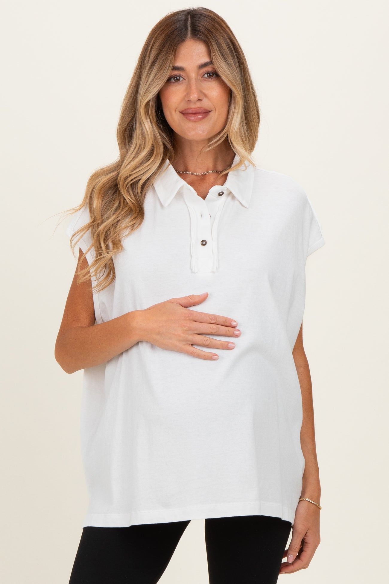 woman wearing a white short sleeve maternity polo shirt and holding her baby bump