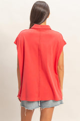 woman wearing a coral oversized short sleeve top with a collared neckline and back seam detail, paired with denim shorts