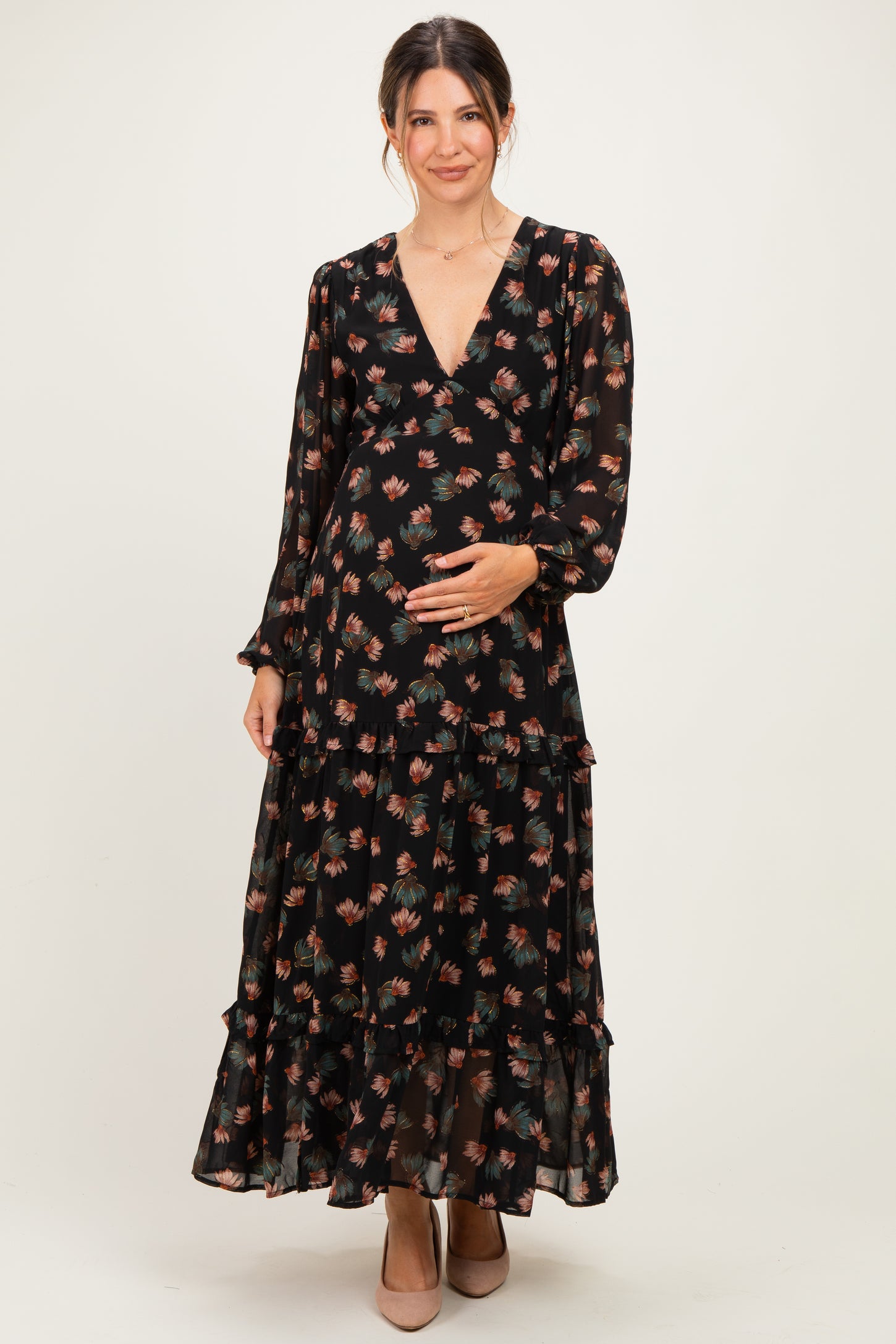 woman wearing a black floral maternity maxi dress with long sleeves and a tiered skirt, holding her baby bump