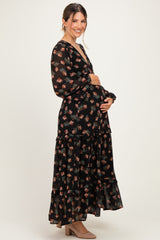 woman wearing a black floral maternity maxi dress with long sleeves and a ruffled hem, cradling her baby bump