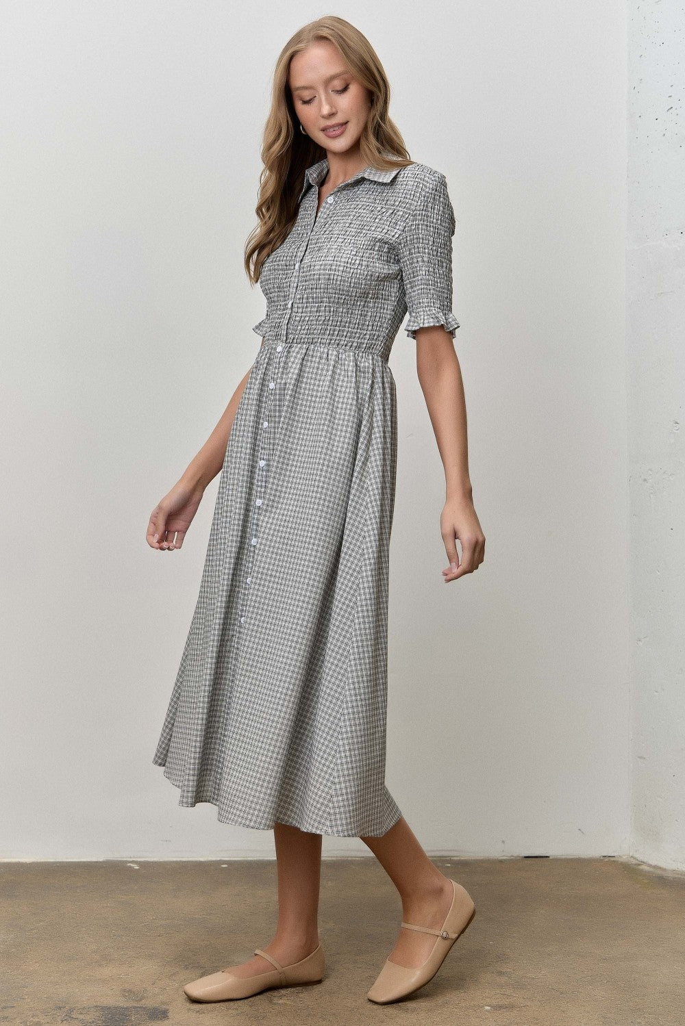 woman wearing a grey and white checkered midi dress with short sleeves and button details, standing on a light background