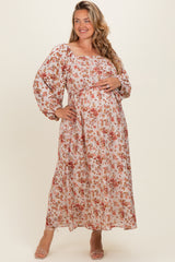 woman wearing a floral maternity maxi dress with long puff sleeves and a fitted waistband, gently cradling her baby bump