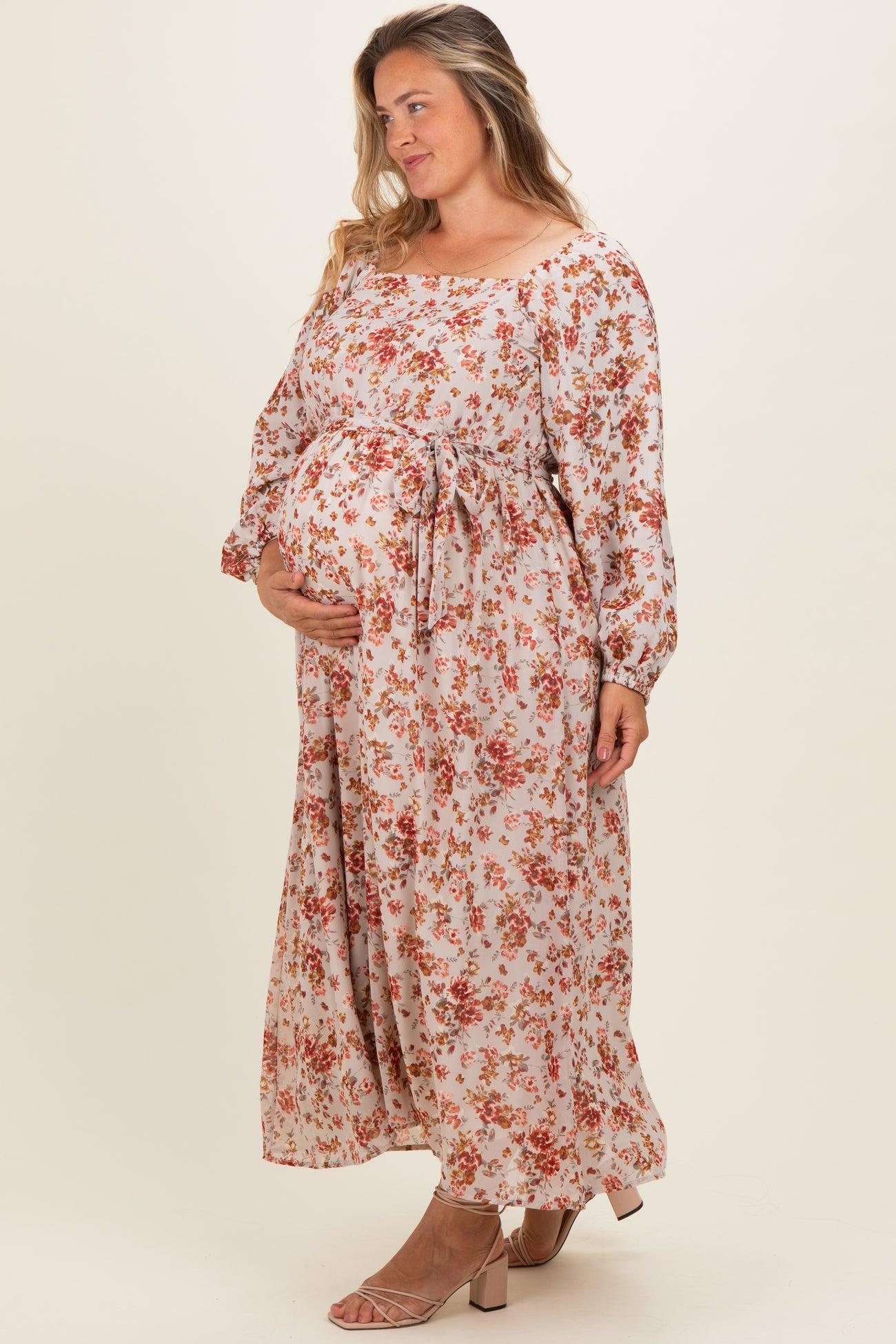 woman wearing a floral maternity plus maxi dress with a tie waist and holding her baby bump