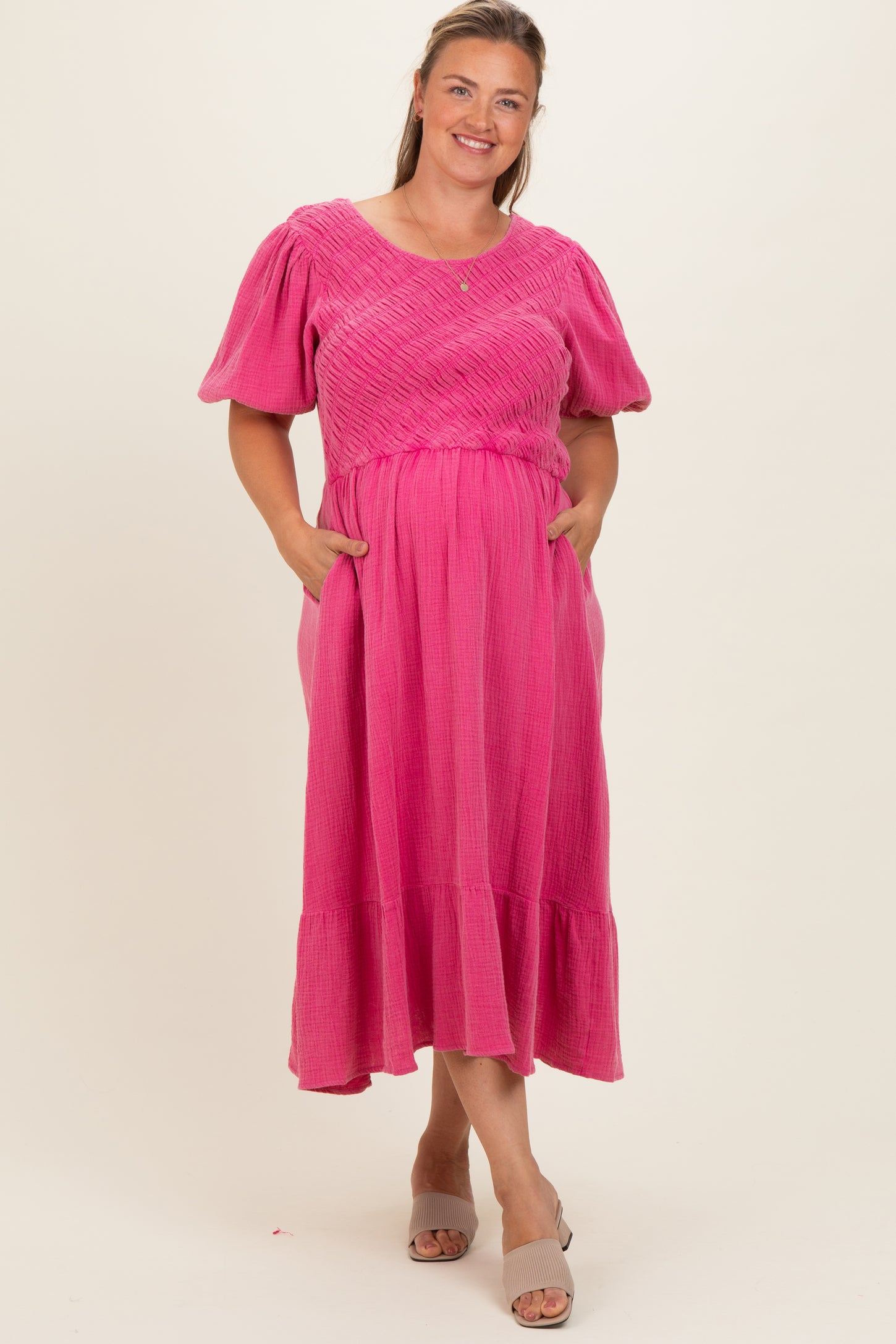woman wearing a pink maternity plus dress with puff sleeves and pockets, standing against a neutral background