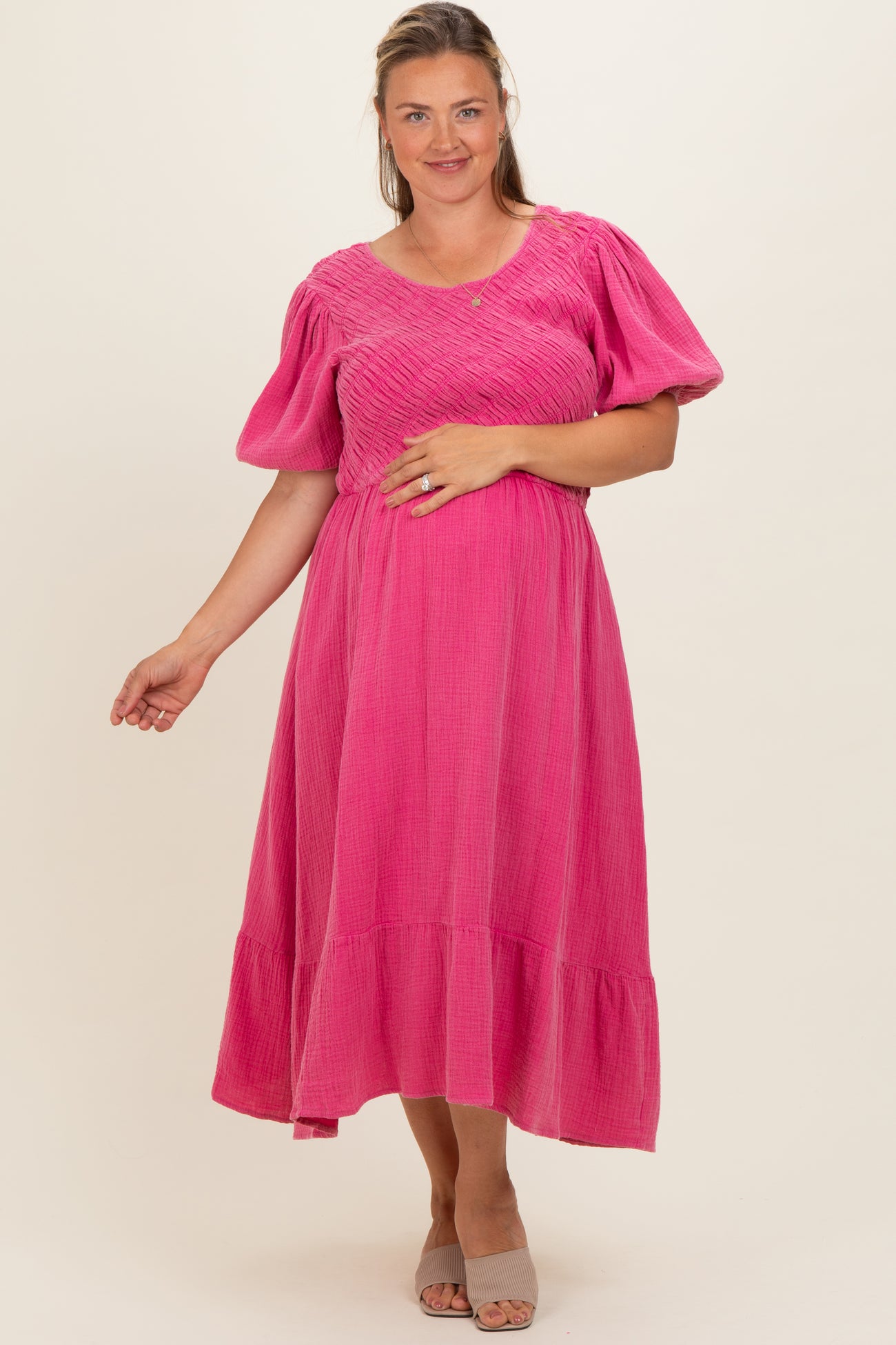 woman wearing a hot pink maternity plus dress with a smocked bodice and puff sleeves, showing her baby bump