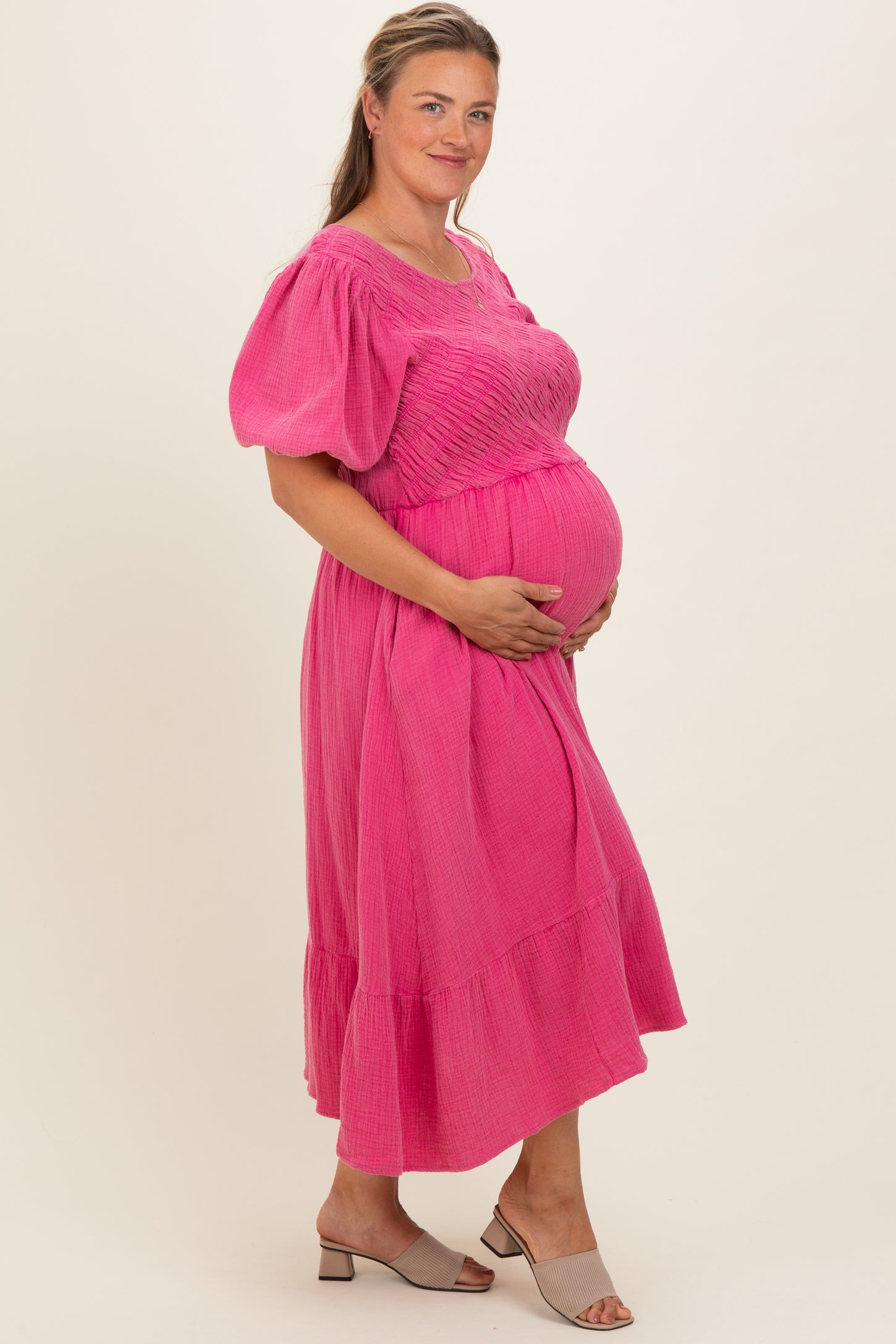 woman wearing a bright pink short sleeve maternity dress with smocked bodice and ruffle hem, holding her baby bump