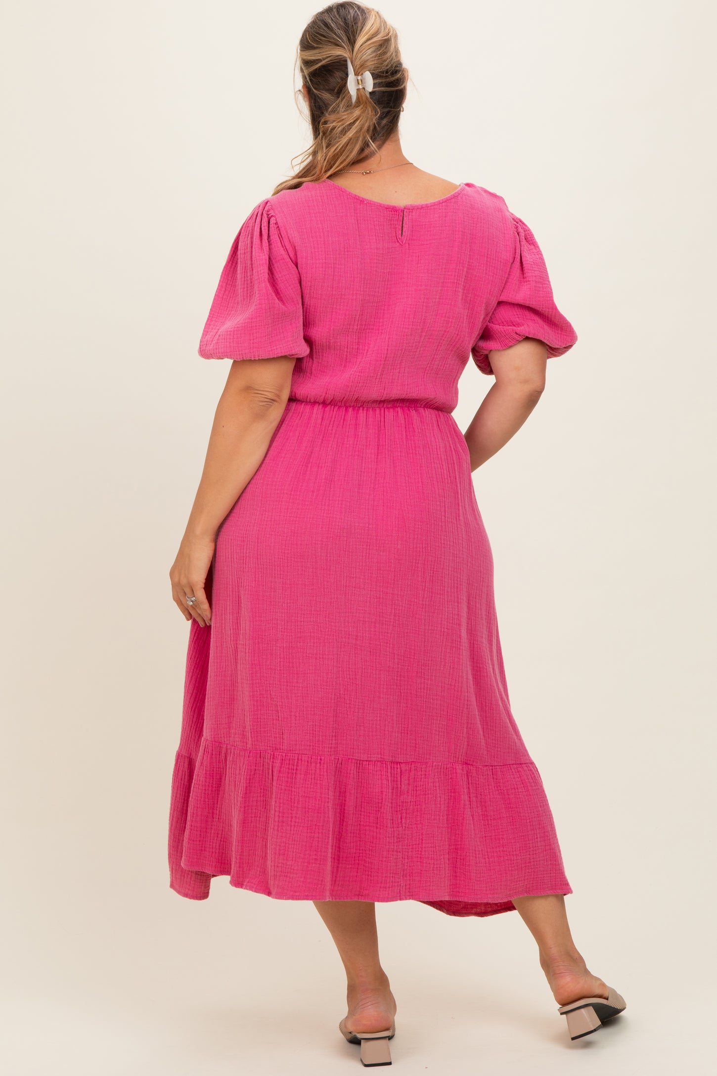 woman wearing a pink maternity plus dress with short puff sleeves and a tiered skirt, showing her back