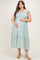 woman wearing a light green maternity plus dress with a smocked bodice and ruffled hem, holding her baby bump