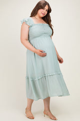 woman wearing a light green maternity plus dress with a smocked bodice and ruffled sleeves, holding her baby bump