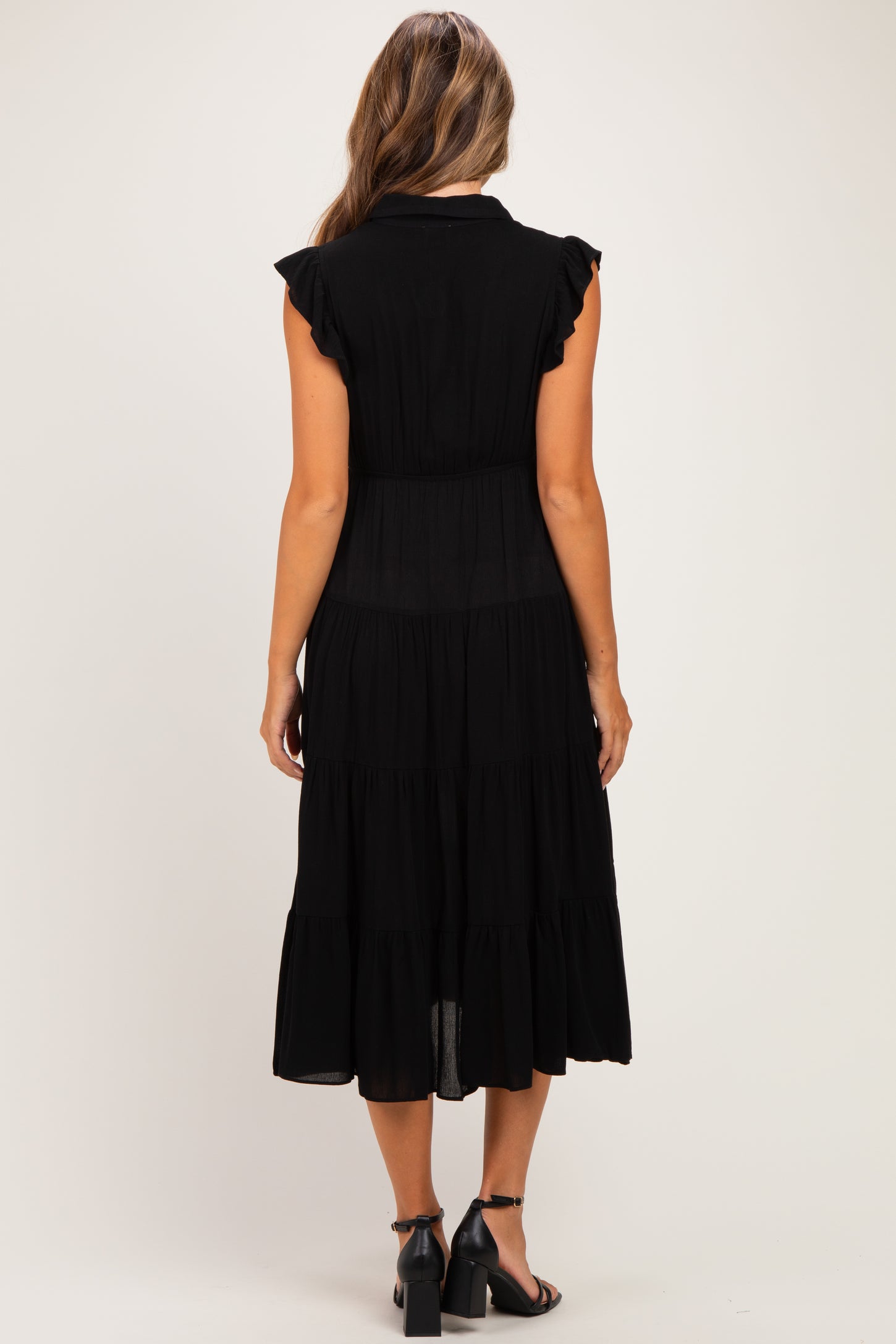 woman wearing a black maxi maternity dress with ruffled sleeves and tiered skirt, viewed from the back