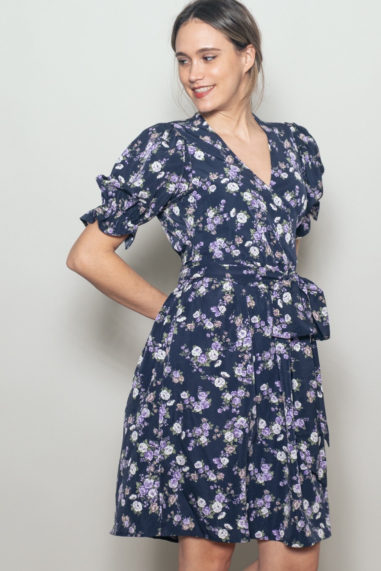 woman wearing a navy blue floral wrap dress with puff sleeves and a self-tie waist belt