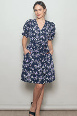 woman wearing a navy blue floral wrap dress with puff sleeves and pockets, accessorized with heels
