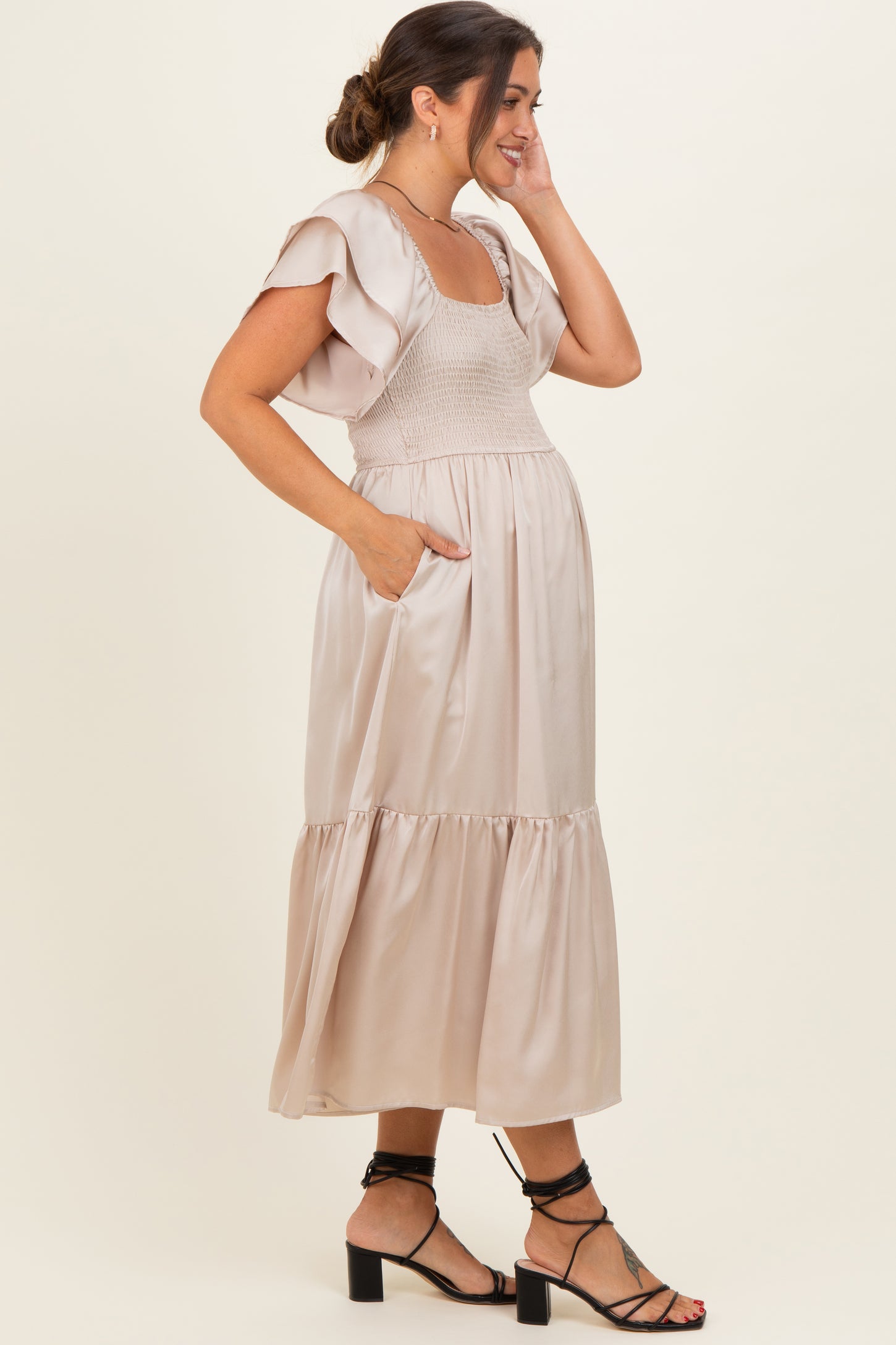 woman wearing a beige maternity dress with tiered skirt, puff sleeves, and side pockets, showing her baby bump