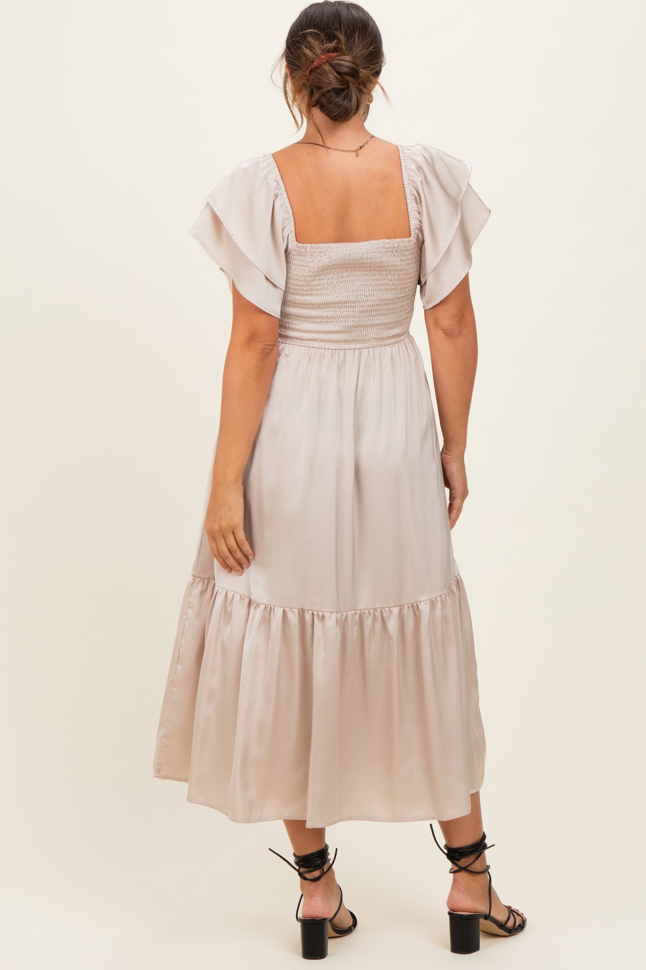 woman wearing a beige maternity dress with a smocked bodice and flutter sleeves, viewed from the back