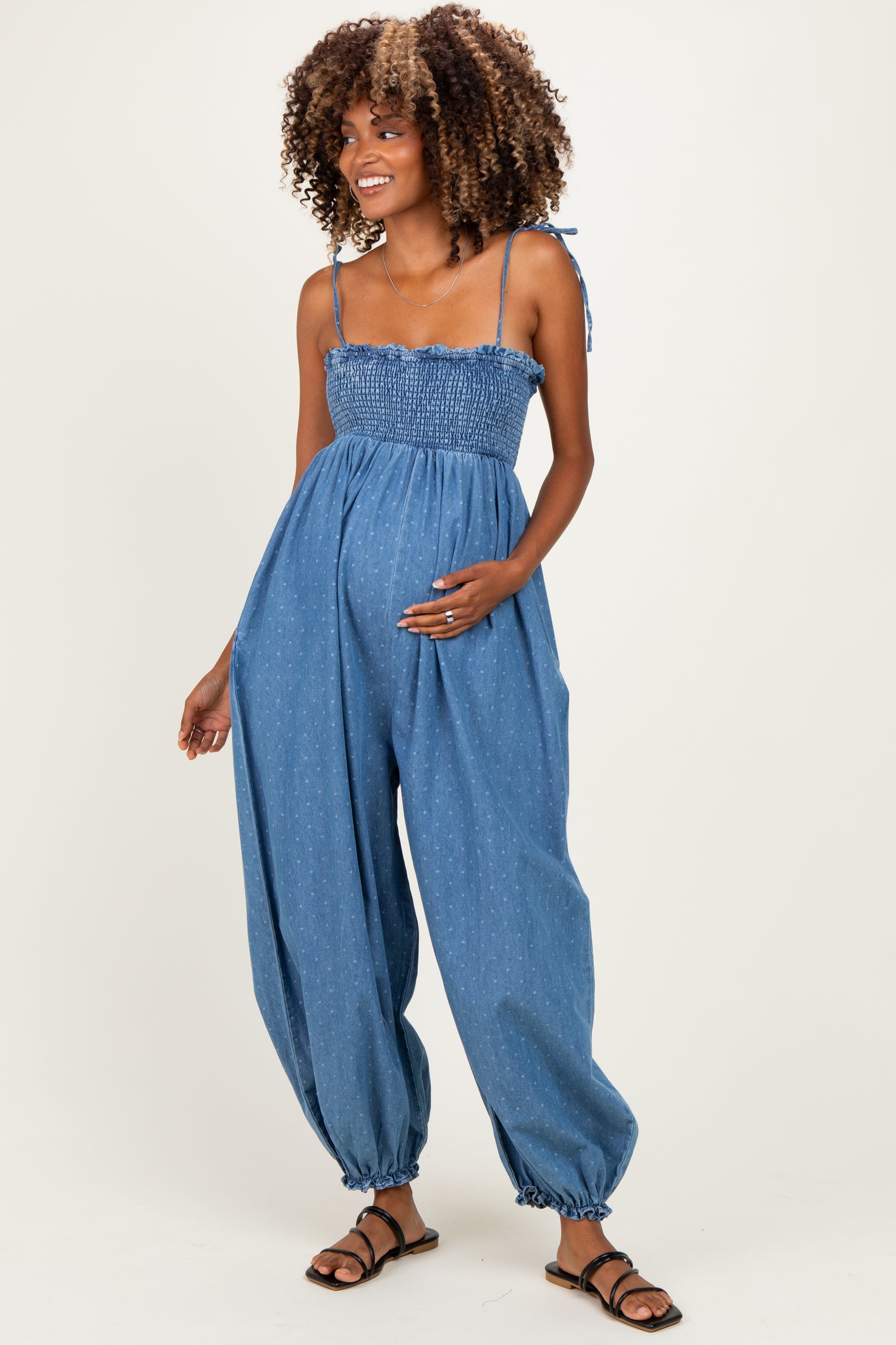 woman wearing a denim maternity jumpsuit with smocked bodice and balloon legs, showing her baby bump
