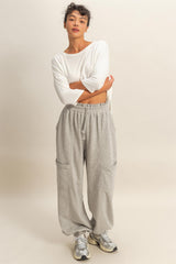 woman wearing a white long sleeve top and gray wide-leg sweatpants with pockets
