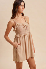 woman wearing a beige ruffled sundress with embroidery details and pockets, standing in profile against a neutral background