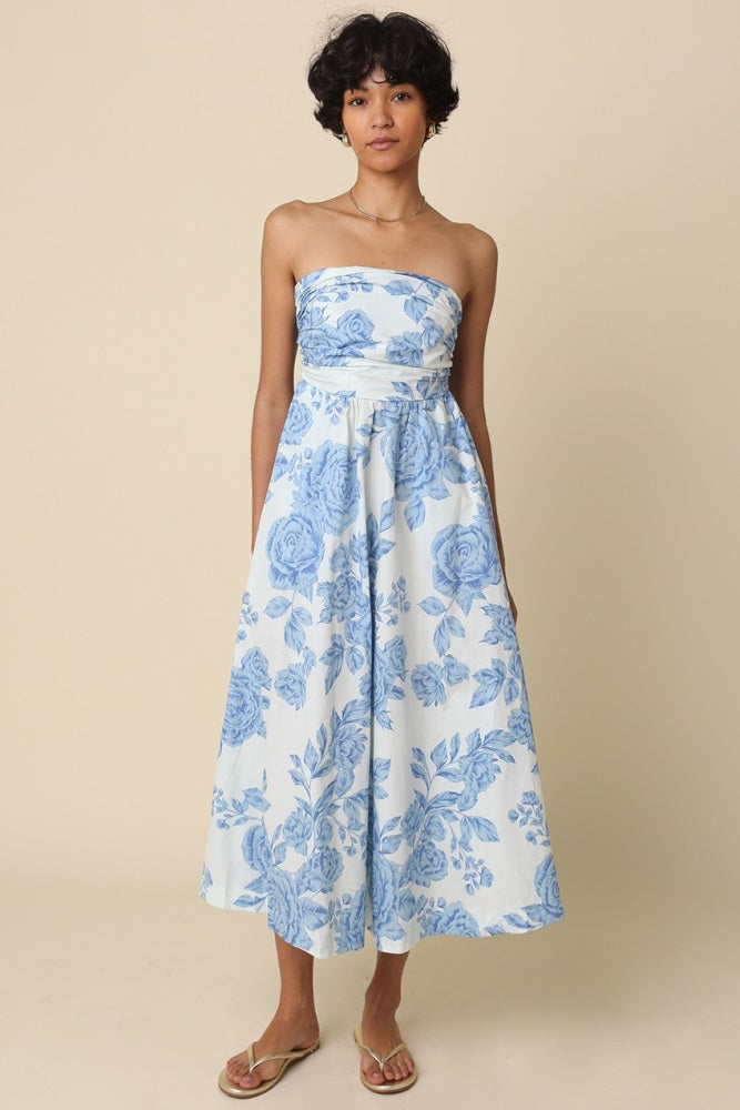 woman wearing a strapless midi dress with a blue floral pattern and a fitted waist, standing against a neutral background
