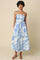 woman wearing a strapless midi dress with a blue floral pattern and a fitted waist, standing against a neutral background