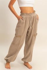 woman wearing beige casual pants with side pockets and an elastic waistband, standing barefoot against a neutral background