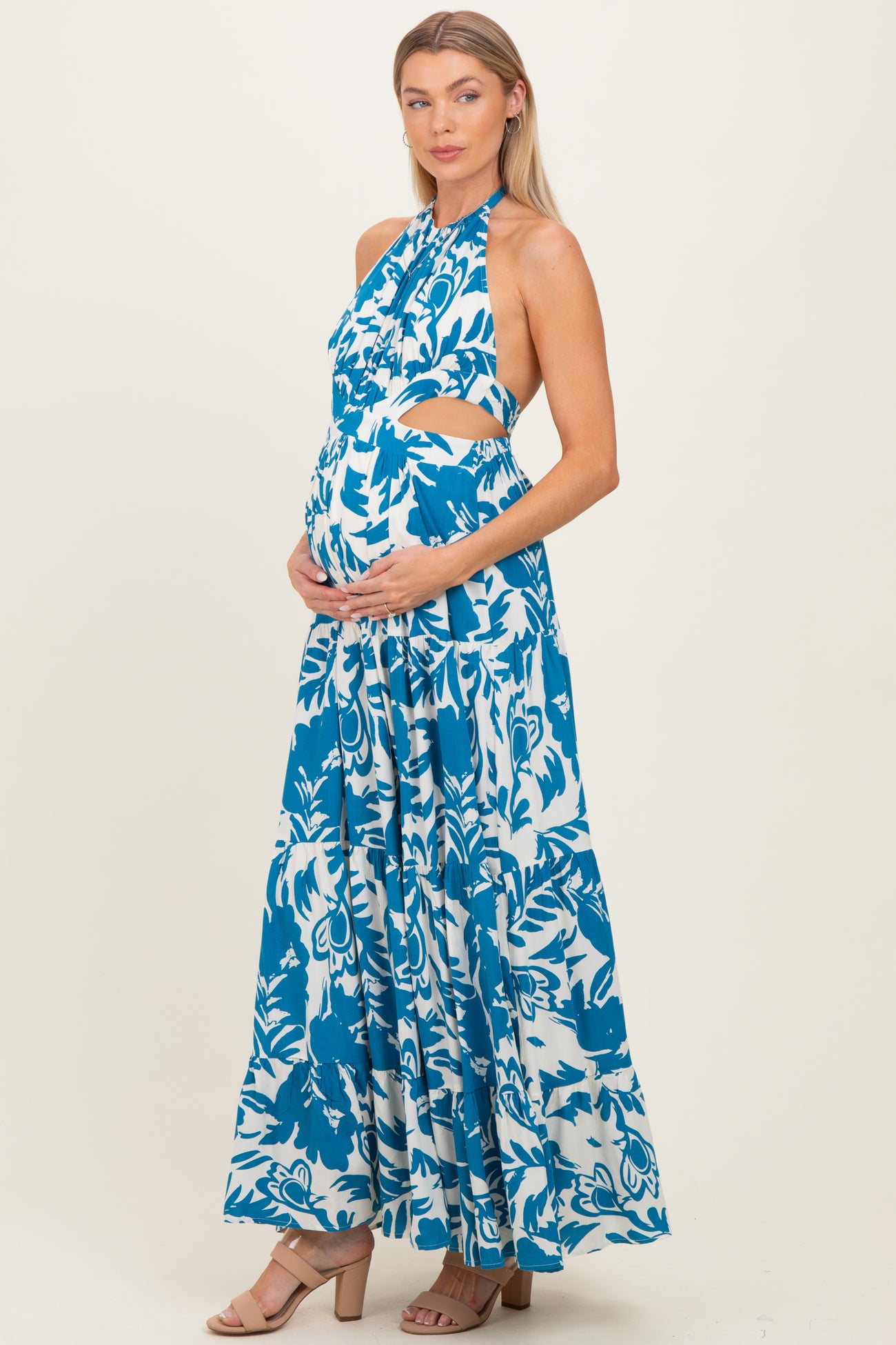 woman wearing a blue and white floral print maternity maxi dress, highlighting her baby bump while posing.