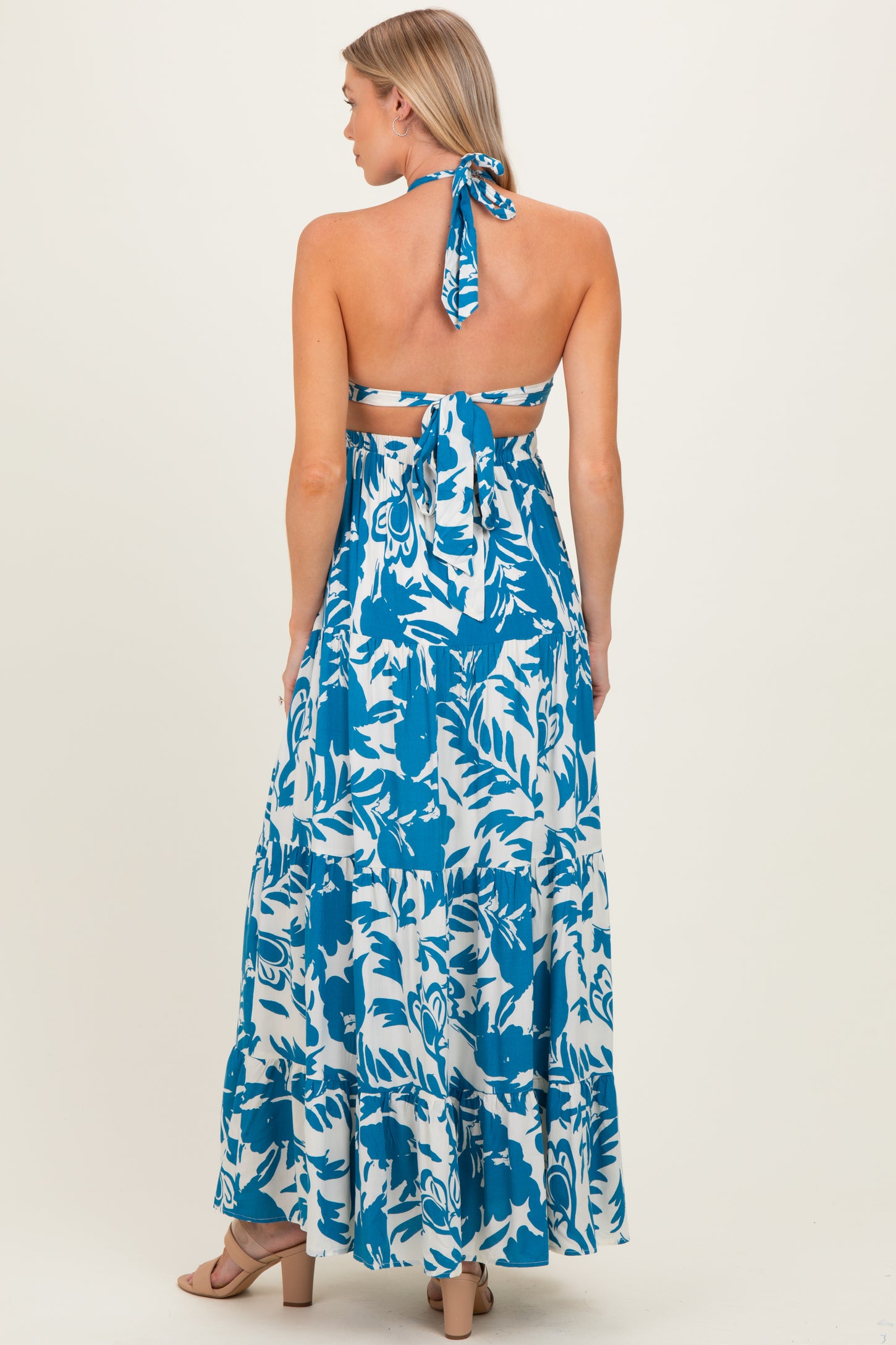 woman wearing a blue and white floral patterned maternity maxi dress with an open back and halter neck detailing