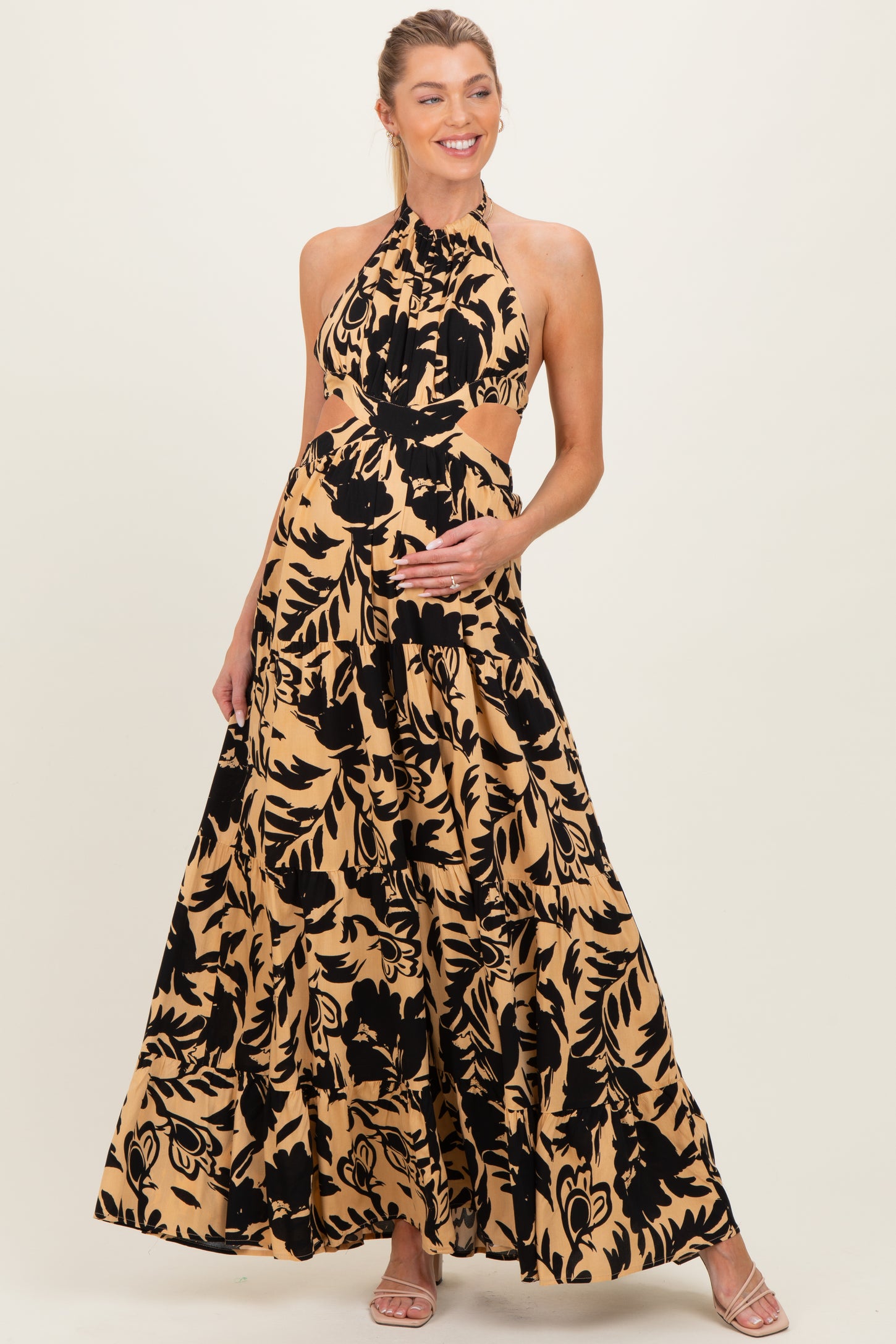 woman wearing a black and tan floral print maternity maxi dress, showing her baby bump with a halter neckline and cut-out details