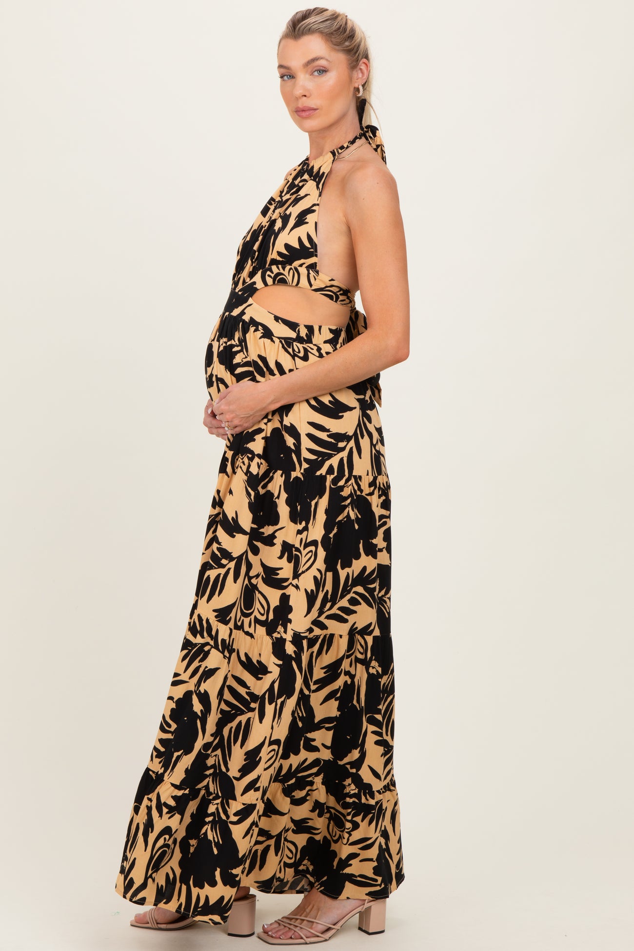 woman wearing a black and beige floral print halter neck maternity maxi dress and cradling her baby bump
