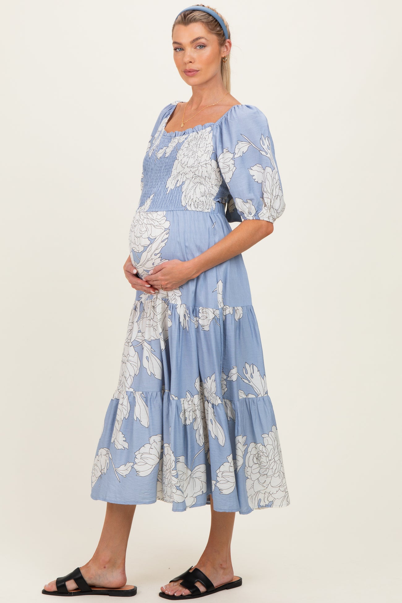 woman wearing a light blue floral maternity dress, showing her baby bump, with puff sleeves and a tiered skirt