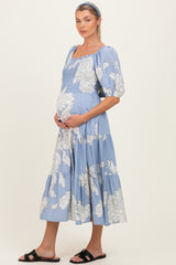 woman wearing a light blue floral maternity dress, showing her baby bump, with puff sleeves and a tiered skirt