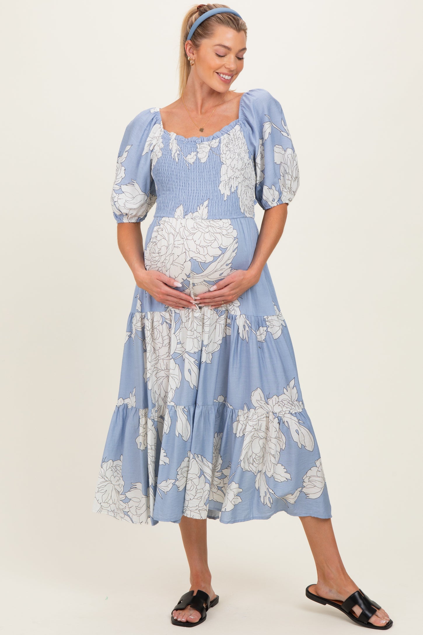 woman wearing a light blue floral maternity dress with puff sleeves, holding her baby bump