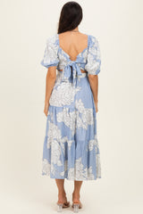 woman wearing a light blue floral midi dress with puff sleeves and a tie-back detail