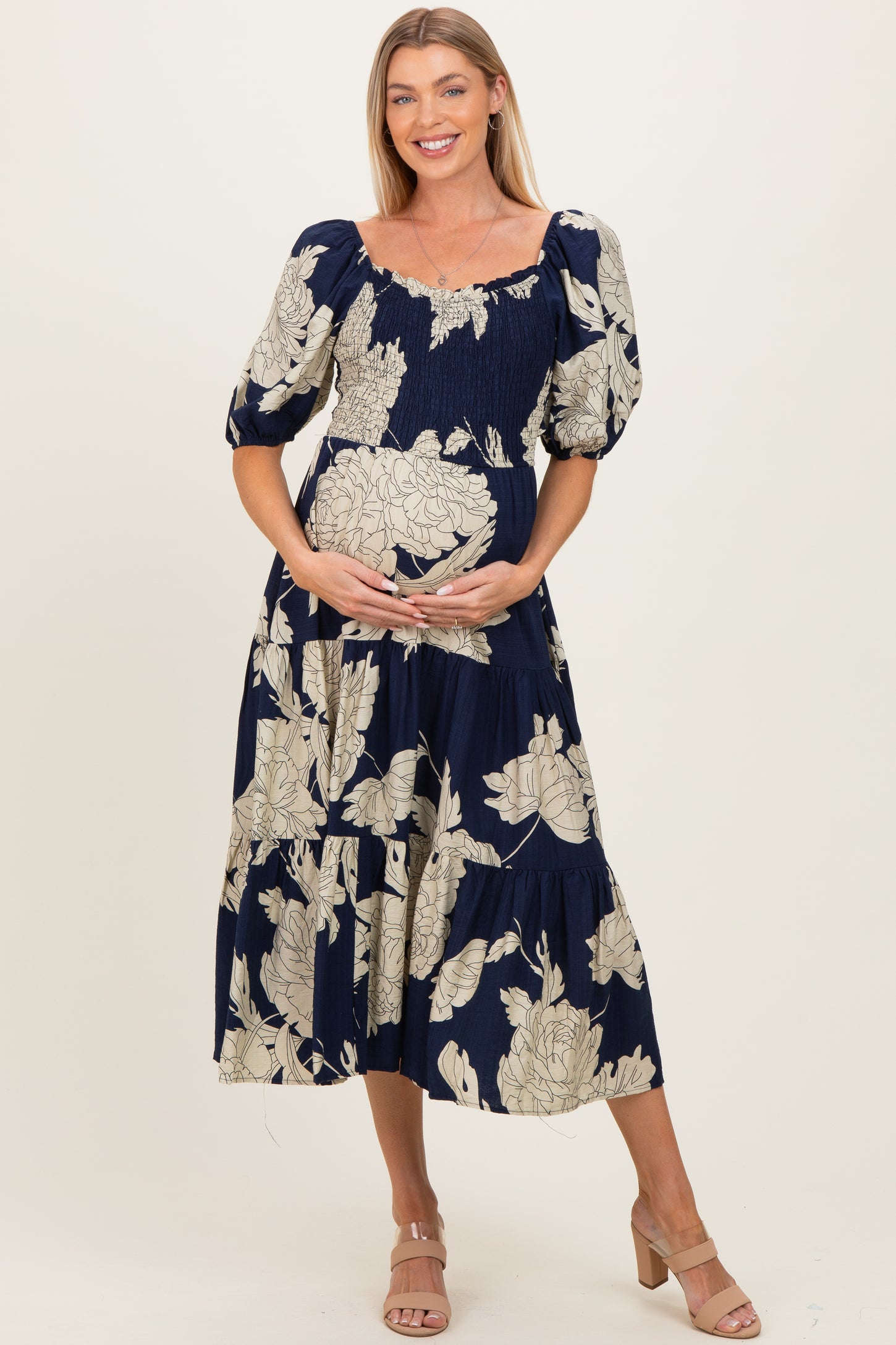 woman wearing a navy blue floral maternity dress with puff sleeves, holding her baby bump