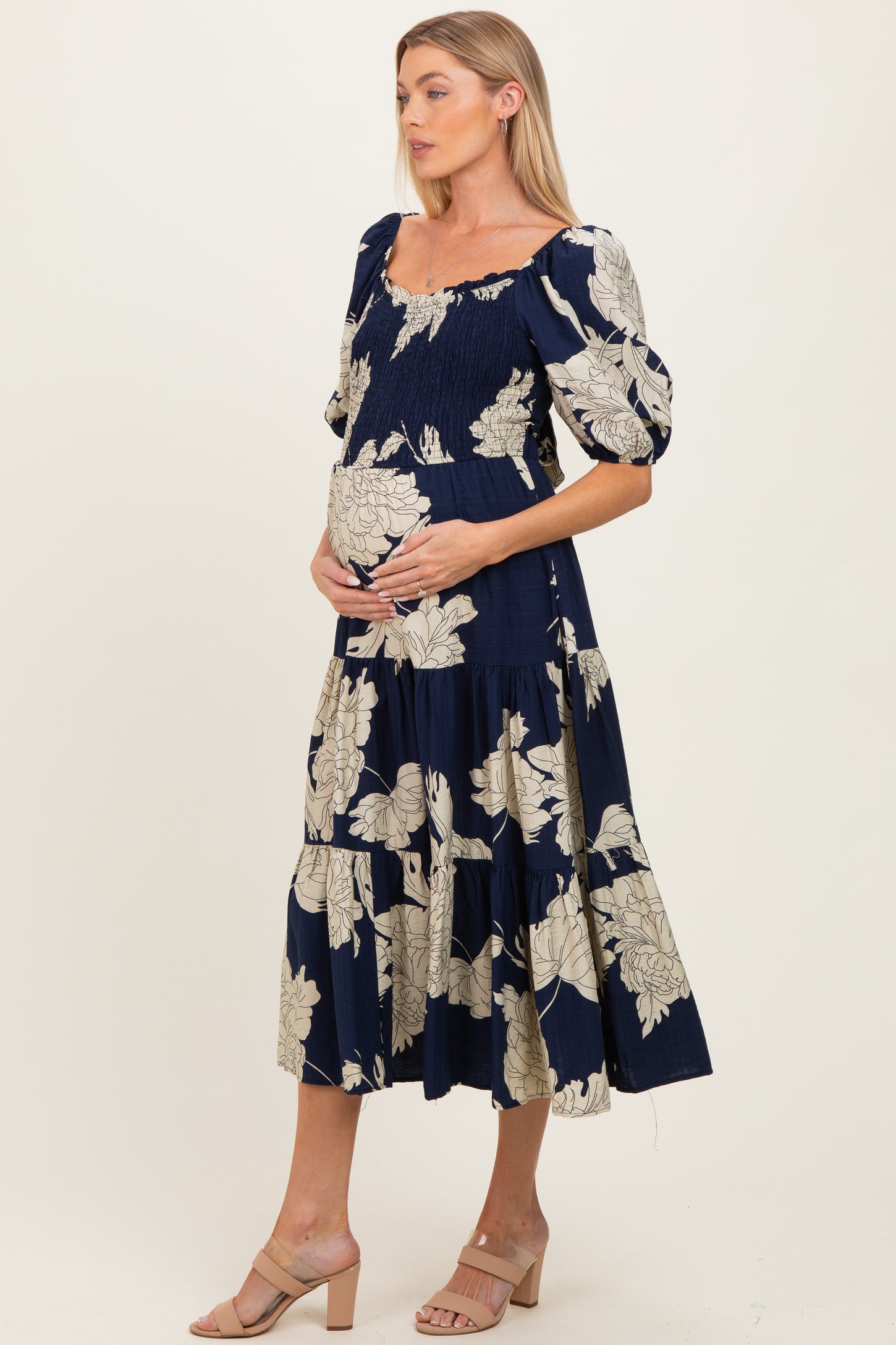 woman wearing a navy floral maternity dress with puff sleeves and a tiered skirt, holding her baby bump