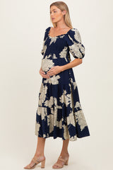 woman wearing a navy floral maternity dress with puff sleeves and a tiered skirt, holding her baby bump