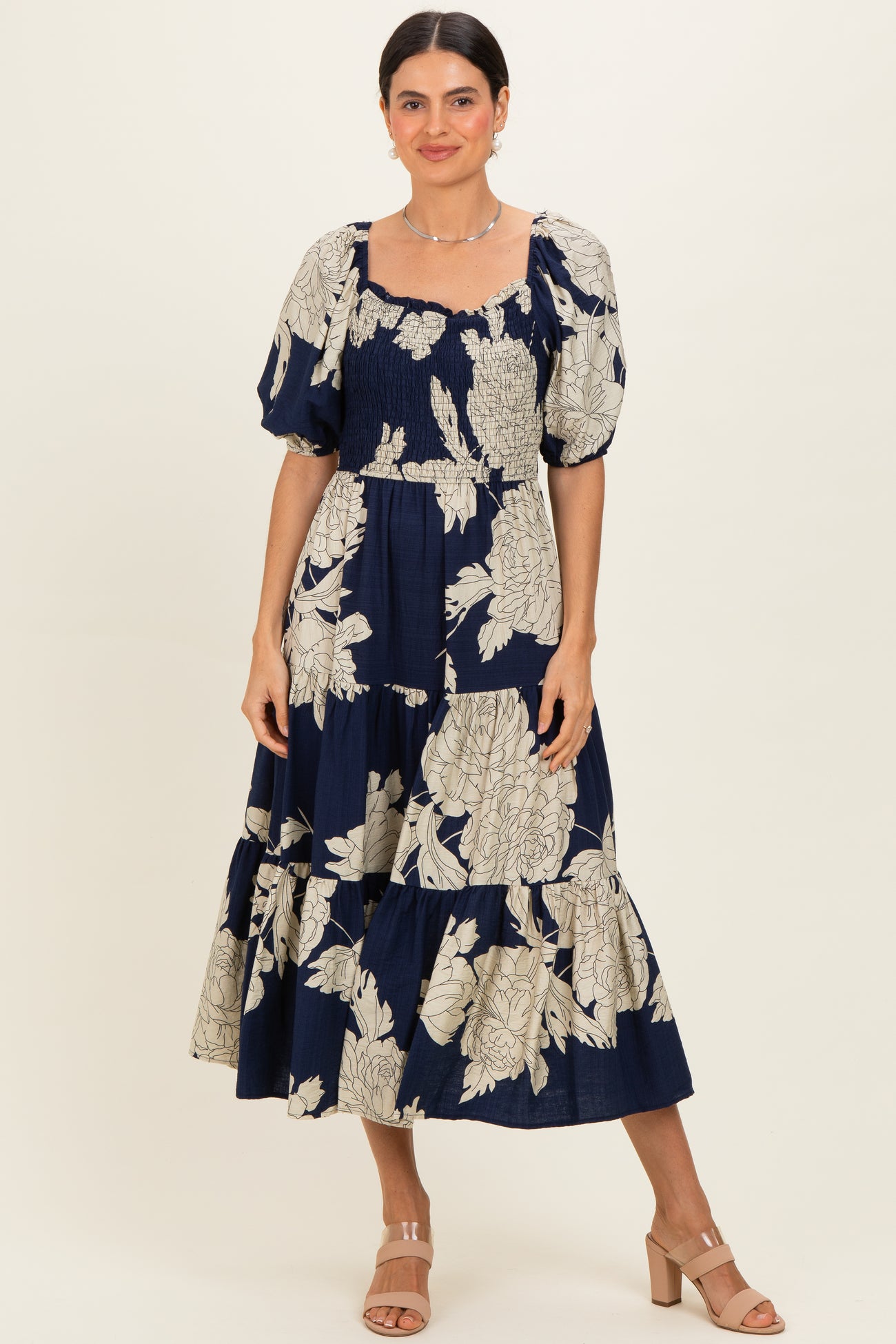 woman wearing a navy blue floral midi dress with puff sleeves and a smocked bodice, standing and smiling