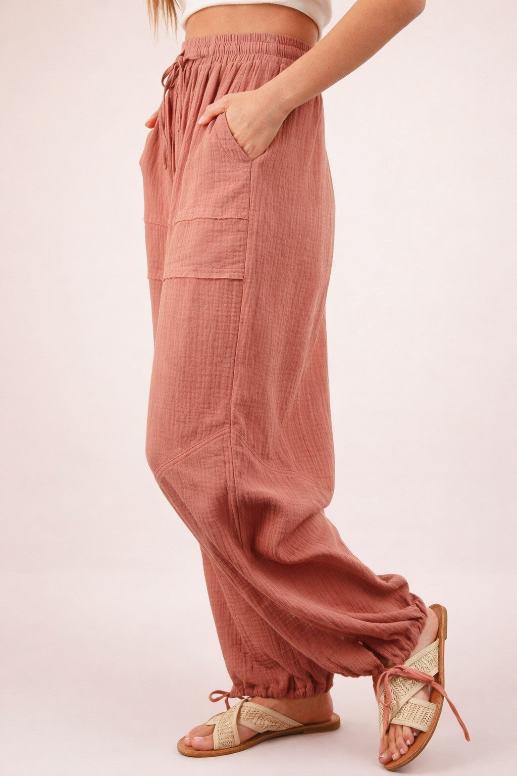 woman wearing blush pink relaxed fit pants with side pockets and elastic cuffs, paired with tan sandals