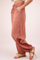 woman wearing blush pink relaxed fit pants with side pockets and elastic cuffs, paired with tan sandals