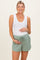 woman wearing a white ribbed maternity tank top and green maternity shorts, showing her baby bump