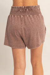 woman wearing brown smocked waist shorts, showing the back view and a relaxed fit
