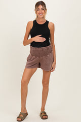 woman wearing a black tank top and brown maternity shorts, holding her baby bump