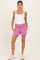 woman wearing a white tank top and pink maternity shorts with pockets, showing a baby bump