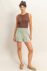 woman wearing a brown sleeveless button-up top and light green smocked shorts
