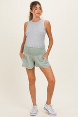 woman wearing a gray sleeveless maternity top and green smocked maternity shorts with side pockets