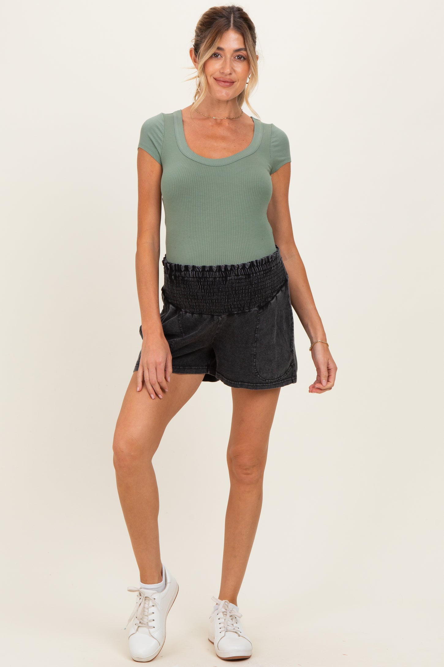 woman wearing a green ribbed scoop neck maternity top and black smocked waist shorts