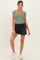 woman wearing a green ribbed scoop neck maternity top and black smocked waist shorts
